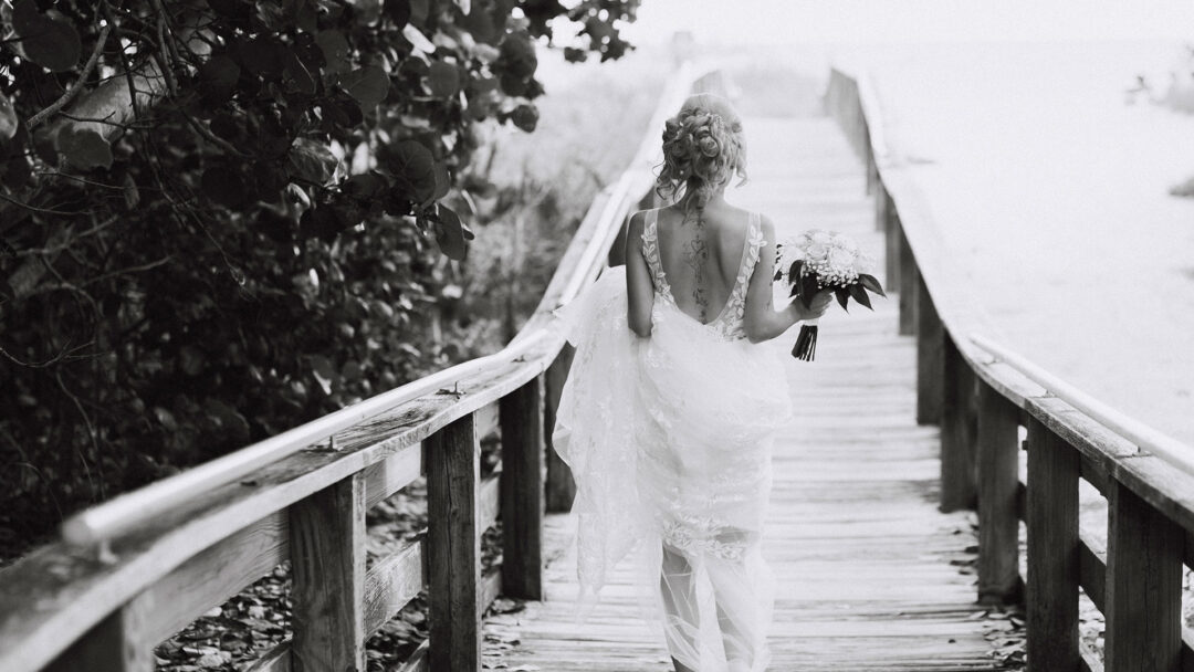 Photo showing bride walking down wooden boardwalk on the beach.